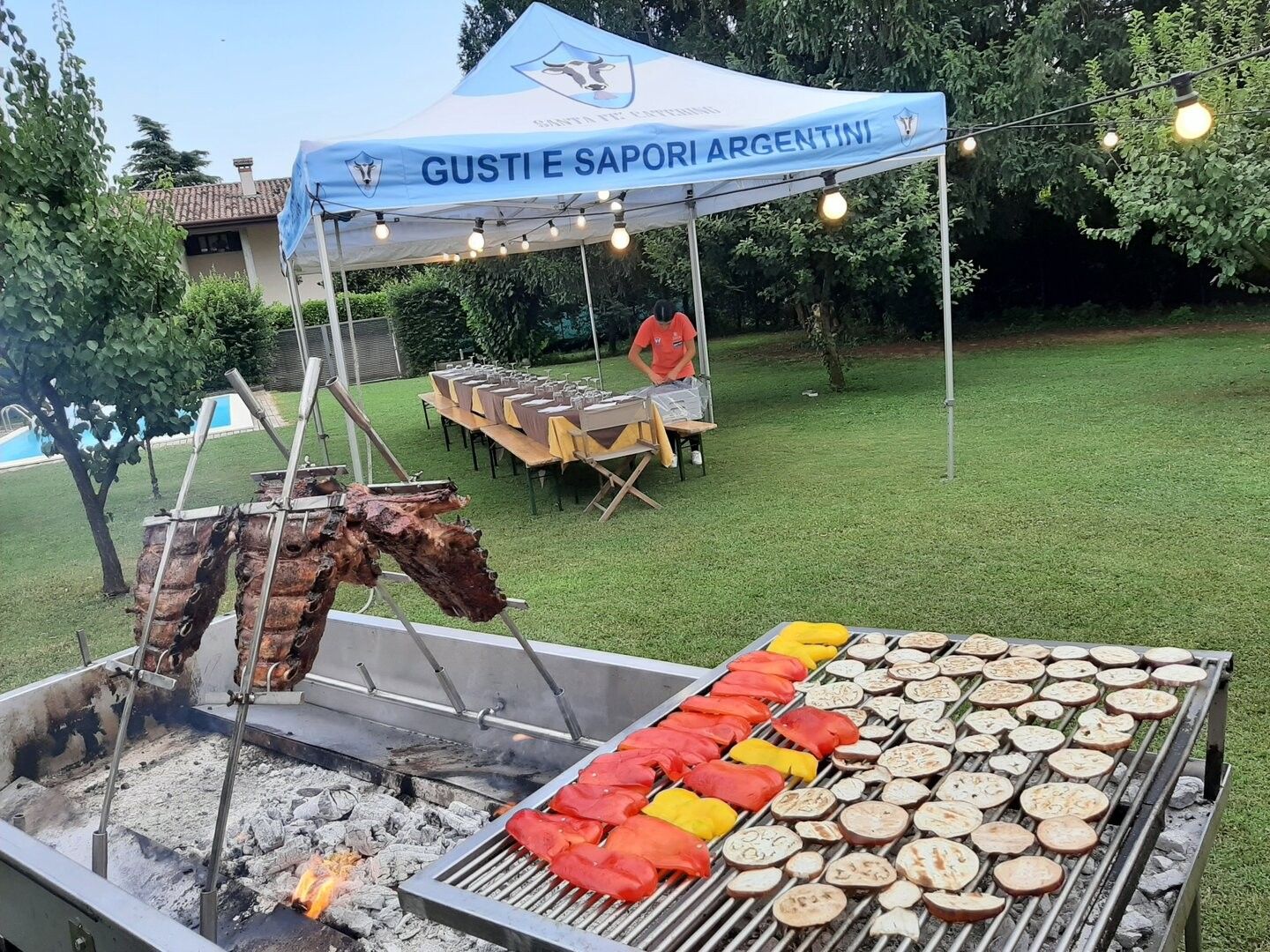 Griglia con costate alla croce e verdure in un giardino, gazebo Santa Fé Catering con luci sullo sfondo