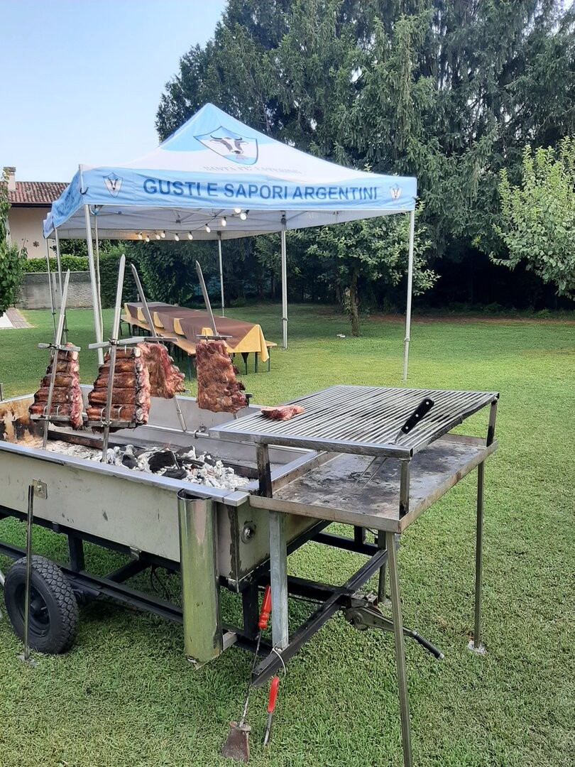 Griglia mobile con asado in un giardino, gazebo Santa Fé Catering sullo sfondo